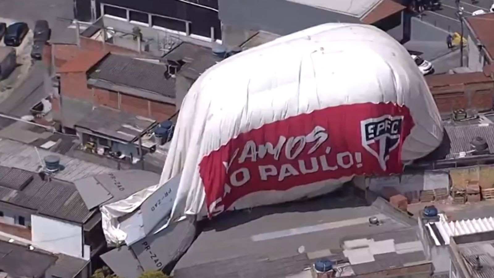 Dirigível cai em telhado de residências. Imagem mostra equipamento sobre telhado e com dizeres do time do São Paulo.