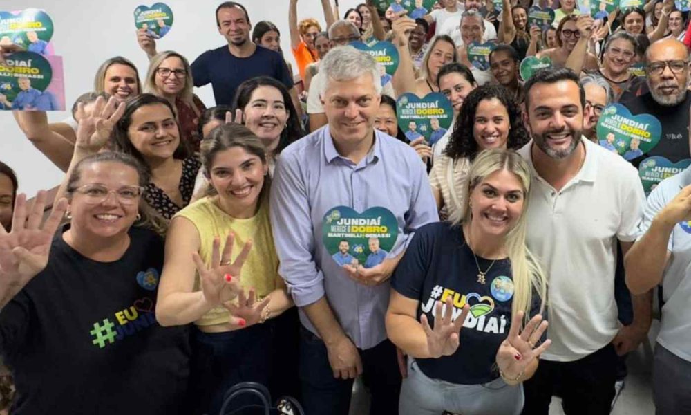 Grupo de educadores e Gustavo Martinelli em reunião de campanha, segurando placas com o slogan "Jundiaí merece o dobro", mostrando apoio