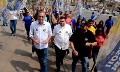 Professor Rodolfo em caminhada ao lado de apoiadores com bandeiras, durante evento público em Várzea Paulista.