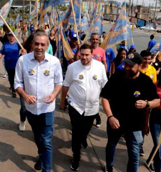 Professor Rodolfo em caminhada ao lado de apoiadores com bandeiras, durante evento público em Várzea Paulista.