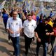 Professor Rodolfo em caminhada ao lado de apoiadores com bandeiras, durante evento público em Várzea Paulista.