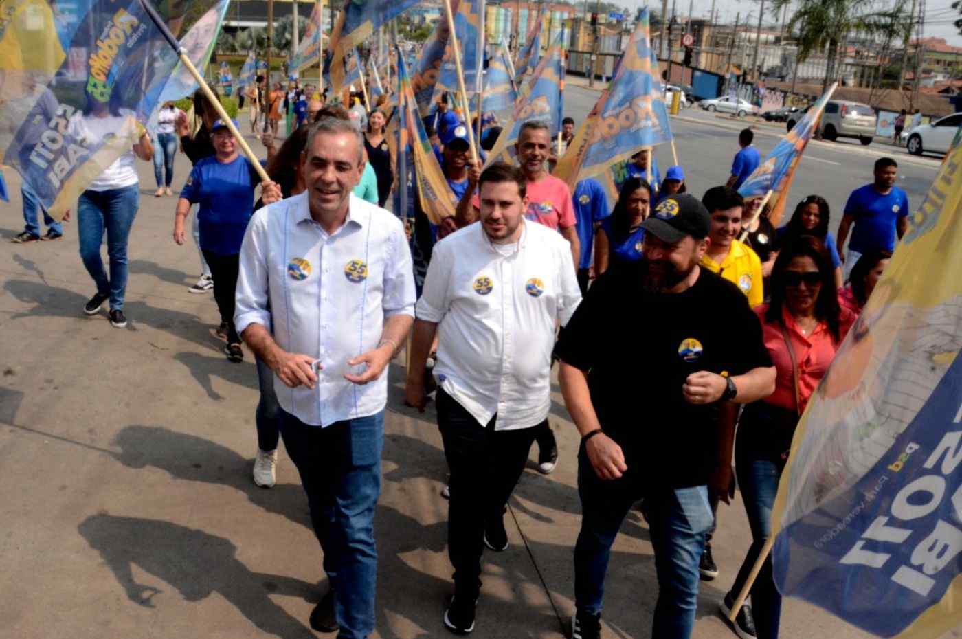 Professor Rodolfo em caminhada ao lado de apoiadores com bandeiras, durante evento público em Várzea Paulista.