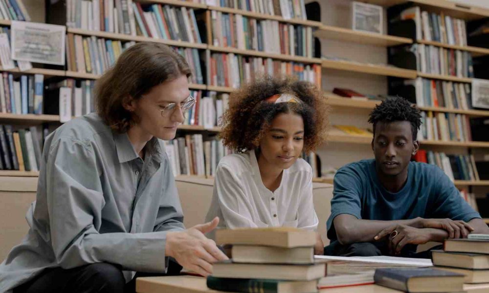 Universidades públicas de São Paulo podem ter mensalidaeds; jovens estão em mesa de biblioteca estudando.