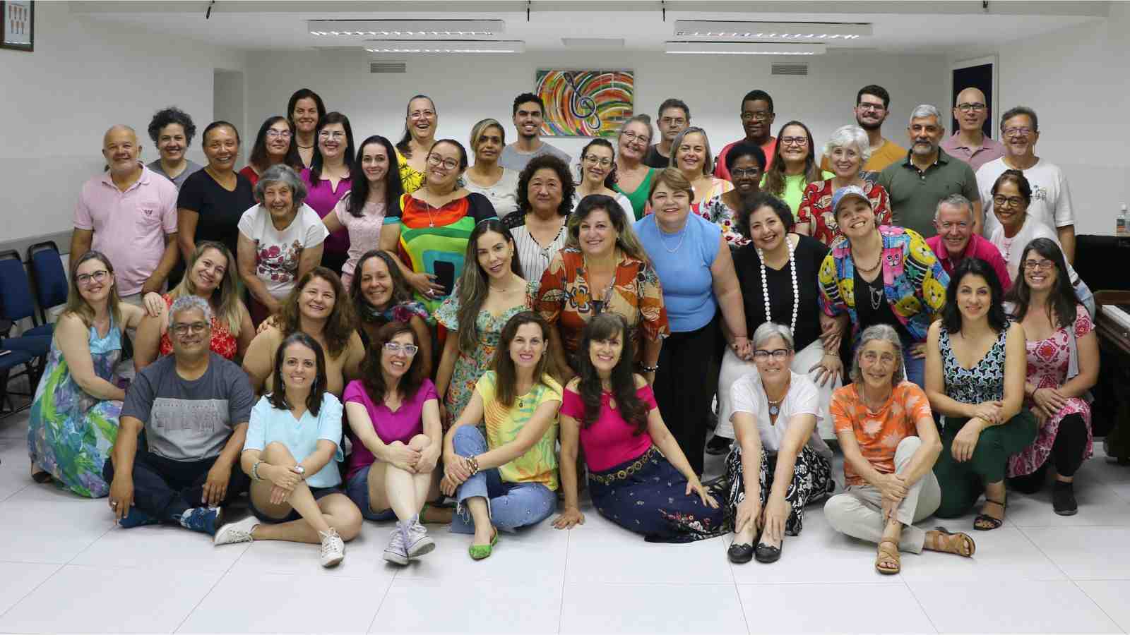 Grupo de coralistas do Colégio Divino Salvador reunidos em uma sala de ensaio, sorrindo e posando para foto em comemoração.