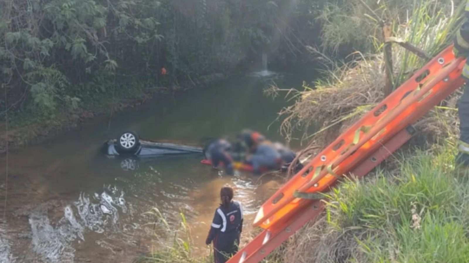 Carro dentro das águas do Rio Jundiaí e equipe de resgate com a vítima.