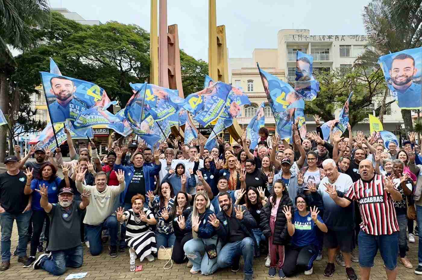 Grupo de apoiadores com bandeiras de Gustavo Martinelli em caminhada no centro de Jundiaí, levantando mãos com o número 44