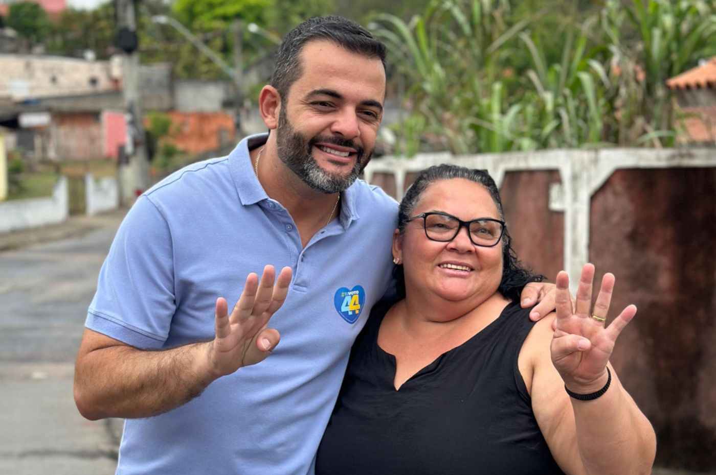 Gustavo Martinelli em caminhada no bairro Ivoturucaia, sorrindo e fazendo gesto de quatro com uma moradora local.