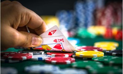 Jogador revelando cartas de Ás e Rei de copas em mesa de cassino com várias fichas coloridas ao fundo, representando uma aposta.