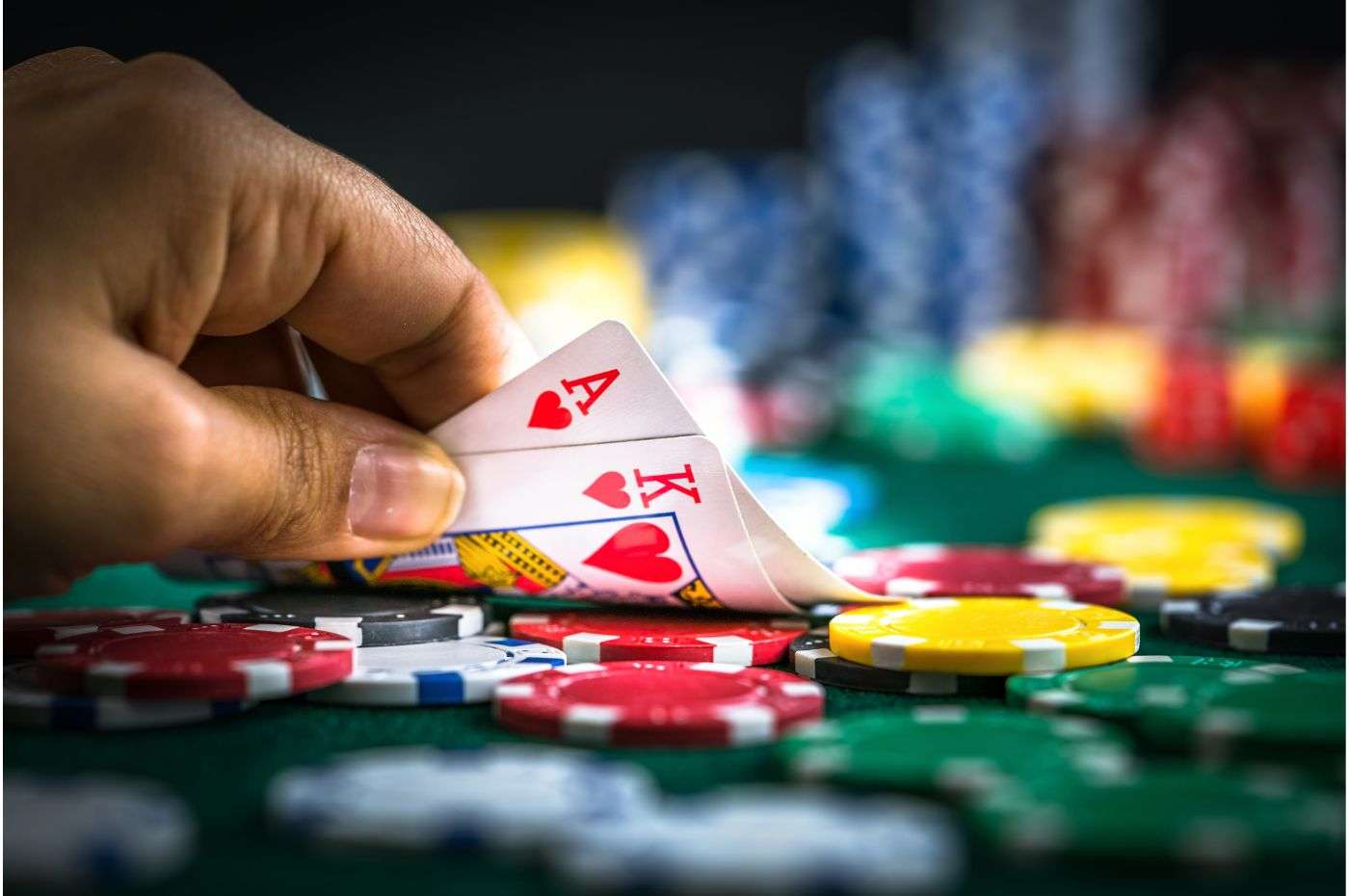 Jogador revelando cartas de Ás e Rei de copas em mesa de cassino com várias fichas coloridas ao fundo, representando uma aposta.