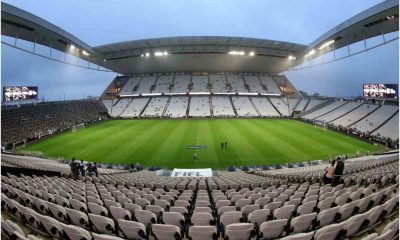 Estádio Neo Química Arena vazio com cadeiras brancas, gramado bem cuidado e iluminação ligada antes de uma partida de futebol.