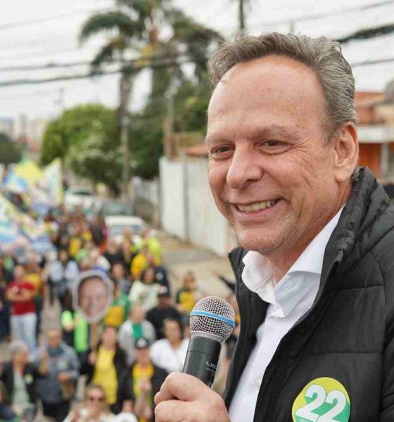 José Antonio Parimoschi segurando microfone e sorrindo durante caminhada de campanha em Jundiaí, cercado por apoiadores com bandeiras.