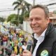 José Antonio Parimoschi segurando microfone e sorrindo durante caminhada de campanha em Jundiaí, cercado por apoiadores com bandeiras.