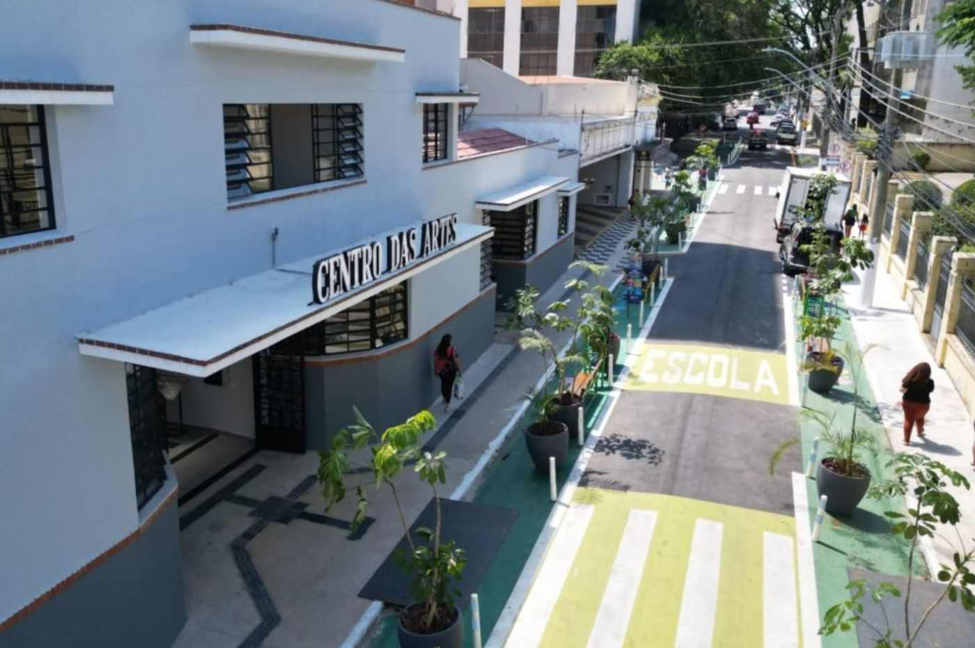 Fachada do Centro das Artes em Jundiaí com calçada acessível, árvores plantadas e área escolar demarcada na rua ao lado.