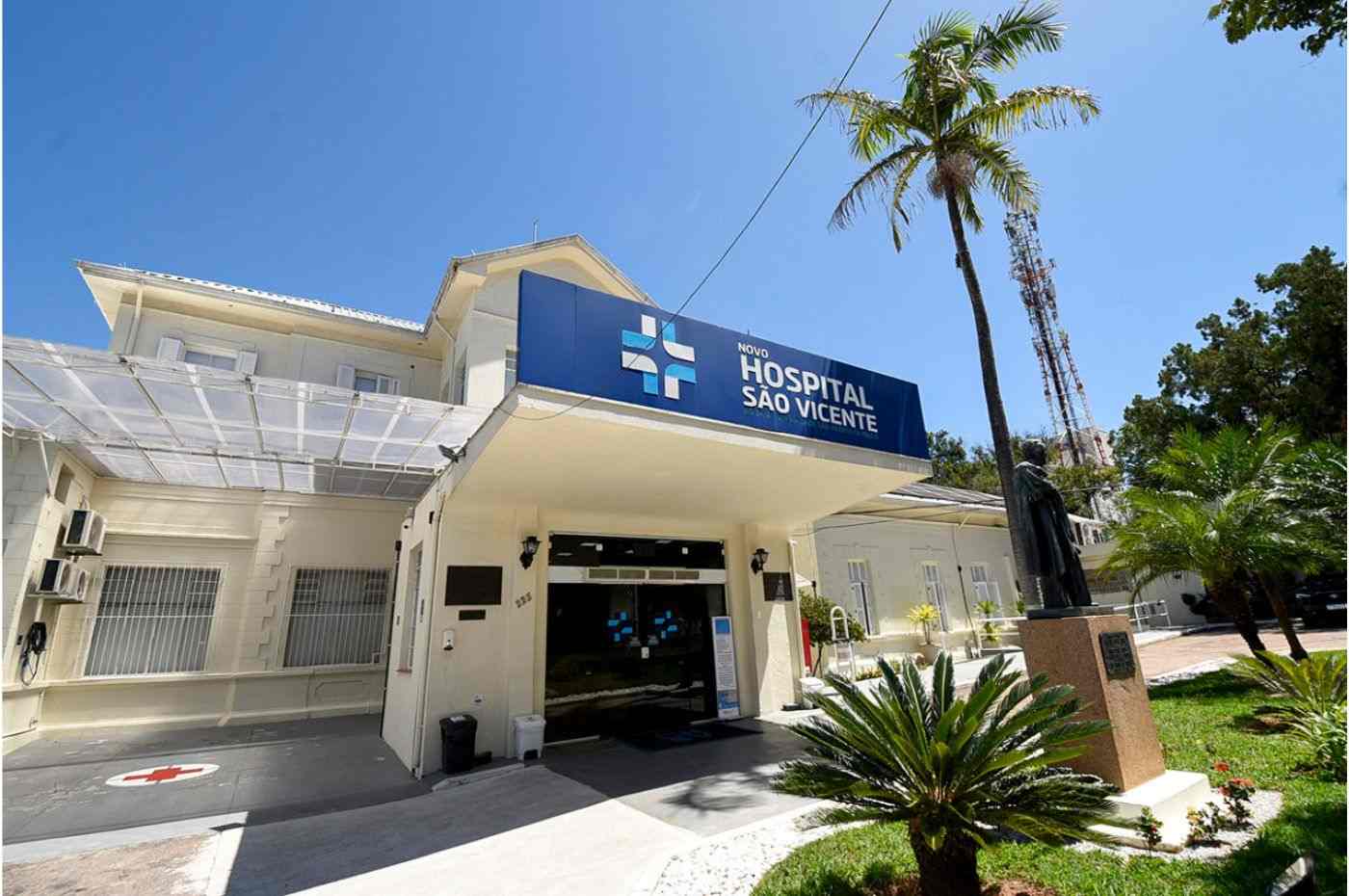 Entrada do Novo Hospital São Vicente em Jundiaí, com fachada moderna, jardim e estátua, sob céu azul e palmeira ao lado.