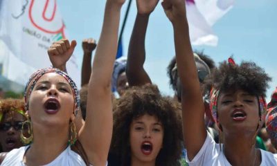 Jovens mulheres afro-brasileiras levantam o punho em protesto, simbolizando a valorização da herança africana, tema da redação do Enem 2024.