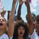 Jovens mulheres afro-brasileiras levantam o punho em protesto, simbolizando a valorização da herança africana, tema da redação do Enem 2024.