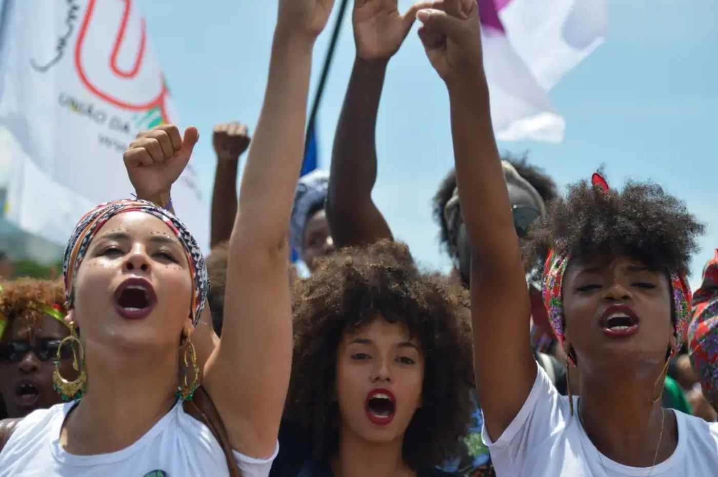 Jovens mulheres afro-brasileiras levantam o punho em protesto, simbolizando a valorização da herança africana, tema da redação do Enem 2024.