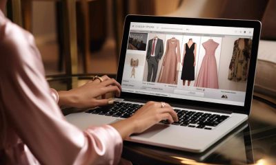 Mulher usando laptop para navegar em site de moda, visualizando opções de roupas e acessórios femininos em ambiente elegante.