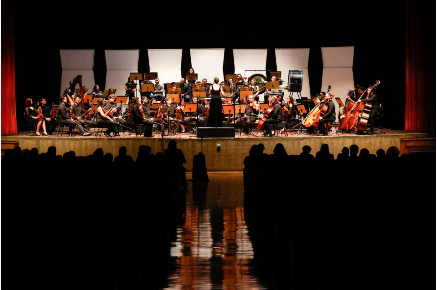 Orquestra Sinfônica Municipal de Jundiaí no Polytheama durante apresentação no palco com músicos tocando instrumentos clássicos, regente ao centro e público assistindo.